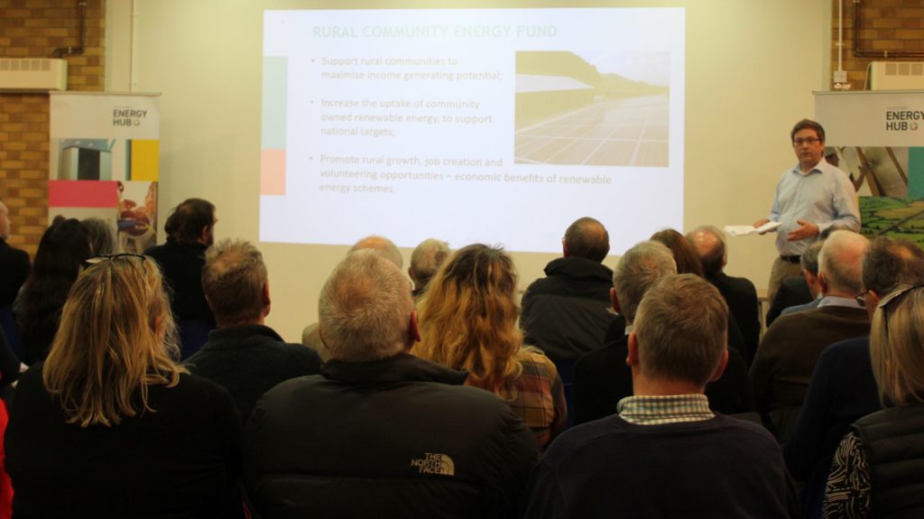 Photograph of a room of people being presented to by a person training at the front of the room, presenting on the "Rural Community Energy Fund"