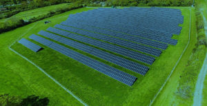 Overhead photograph of a solar farm with lines of solar panels in a green field
