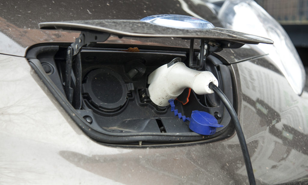 Photograph of an electric car charging port with a power supply charging it.